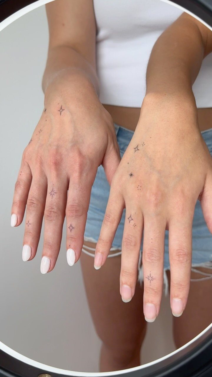 Hands with small fine-line star tattoos on the fingers and back of hand.