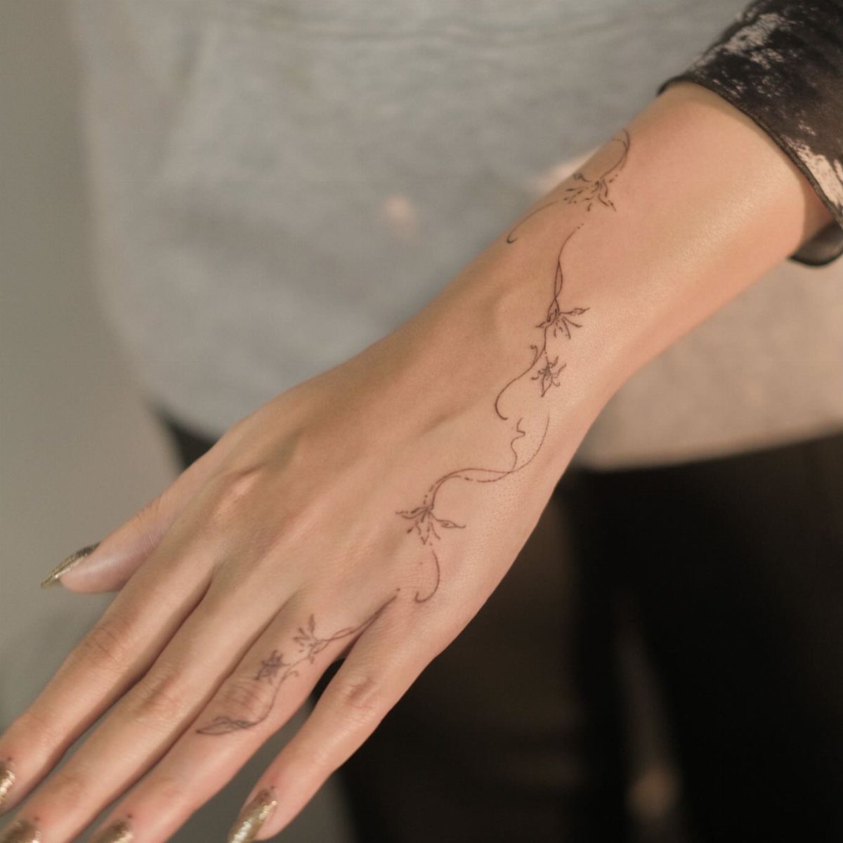 Hand and wrist with a fine-line tattoo of a trailing floral vine.