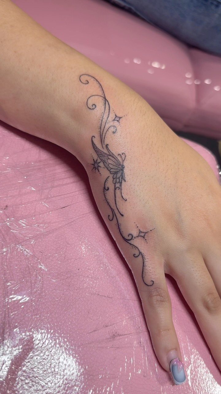 Hand and wrist with a delicate black ink tattoo of swirls and stars