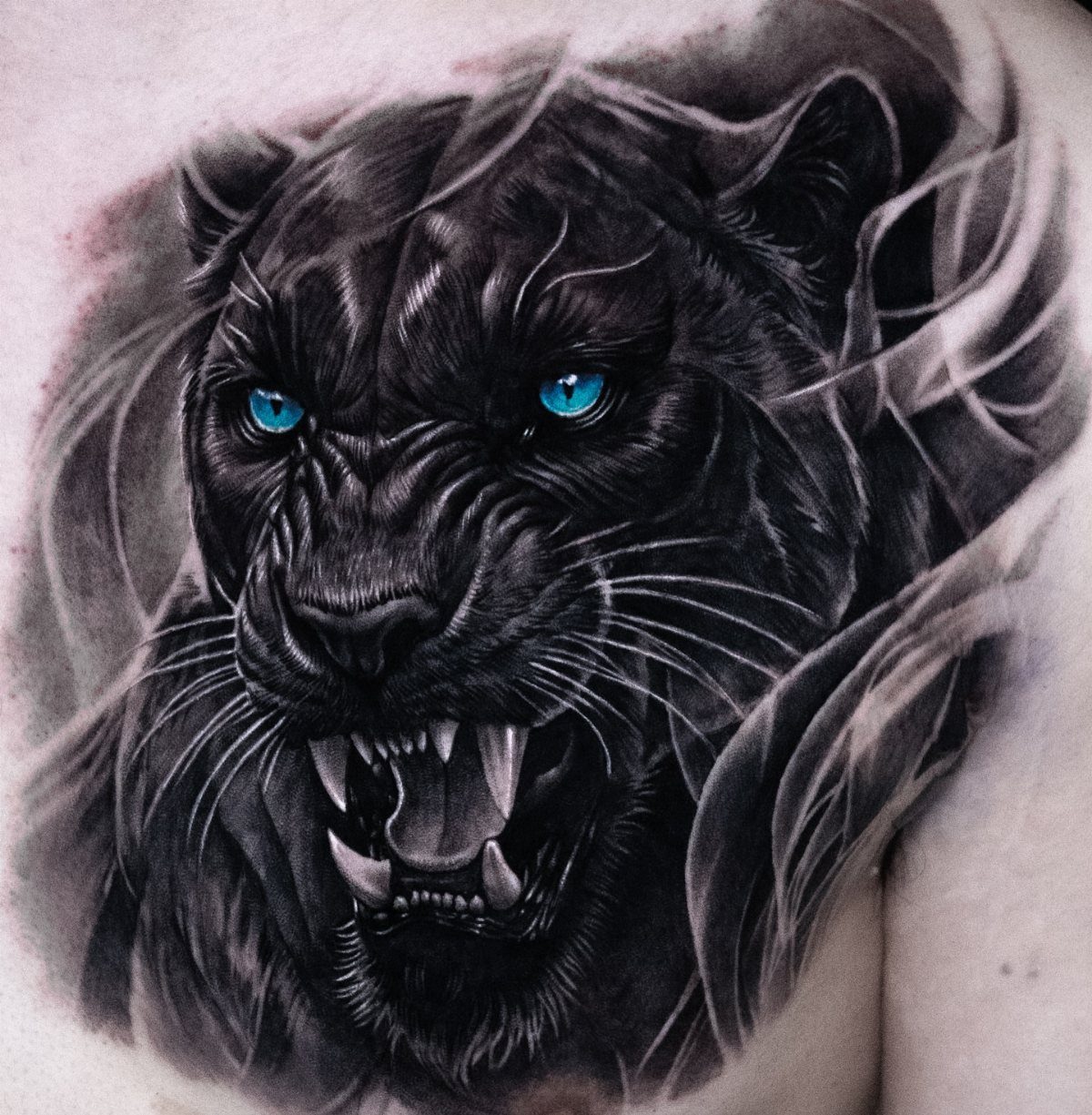 8 Pro Black Tattoos Ideas for Bold, Meaningful Ink 3 Snarling black panther tattoo with bright blue eyes on a person's chest.