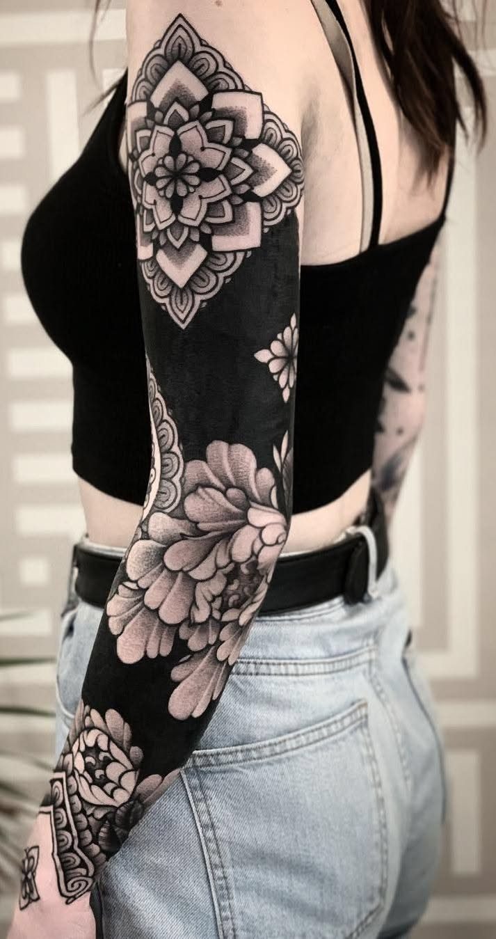 8 Pro Black Tattoos Ideas for Bold, Meaningful Ink 7 Tattoo sleeve with solid black ink, a mandala, and shaded peonies on an arm.