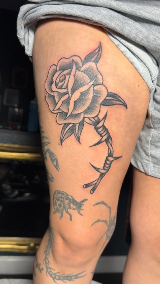 8 Pro Black Tattoos Ideas for Bold, Meaningful Ink 5 Stylized rose tattoo with barbed wire on a person's thigh.