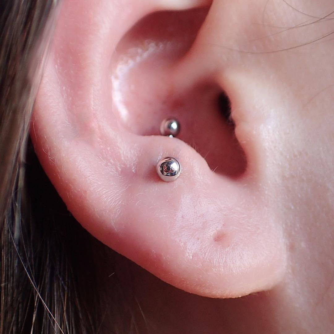 Anti-tragus ear piercing with a silver barbell and small metallic spheres.
