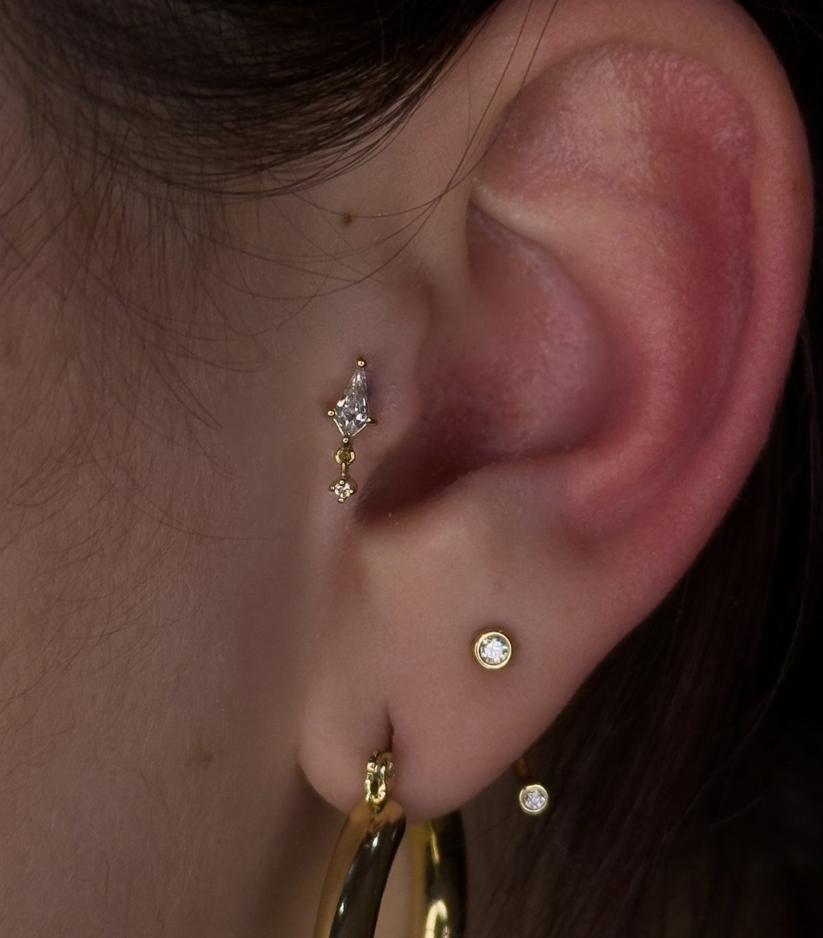 Human ear featuring gold and diamond jewelry, including a unique daith piercing.