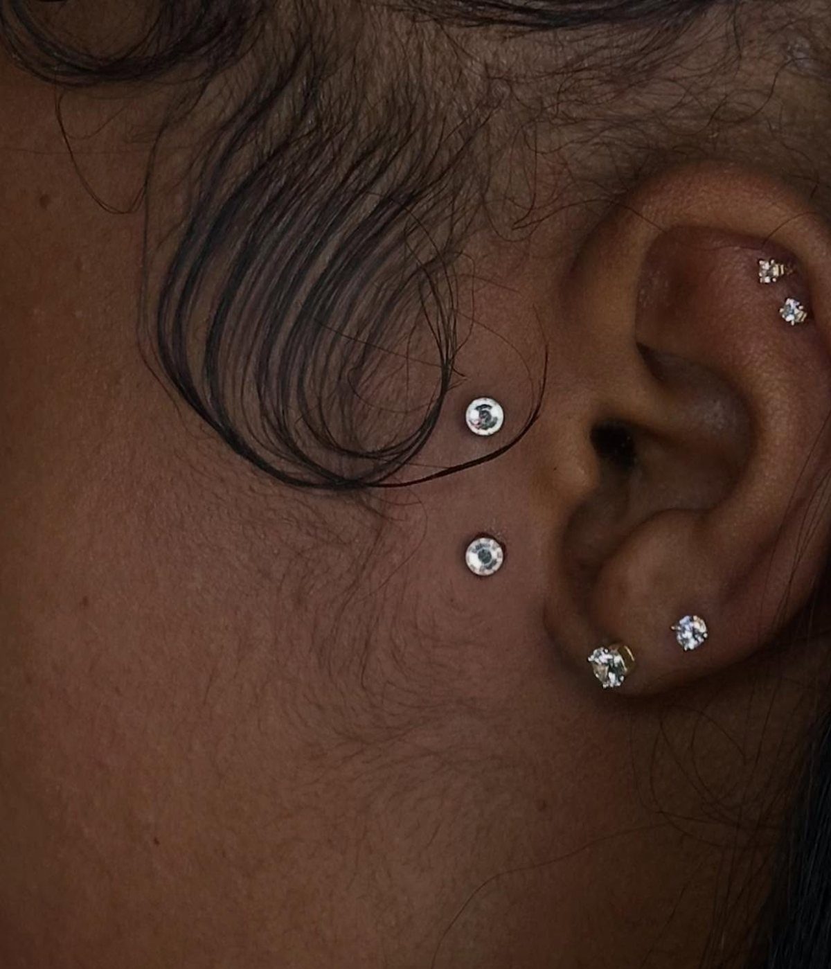 Ear and cheek with multiple diamond stud piercings in rare and unique placements.