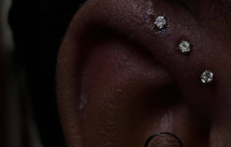 Ear cartilage with three sparkling diamond stud piercings along the upper outer rim.