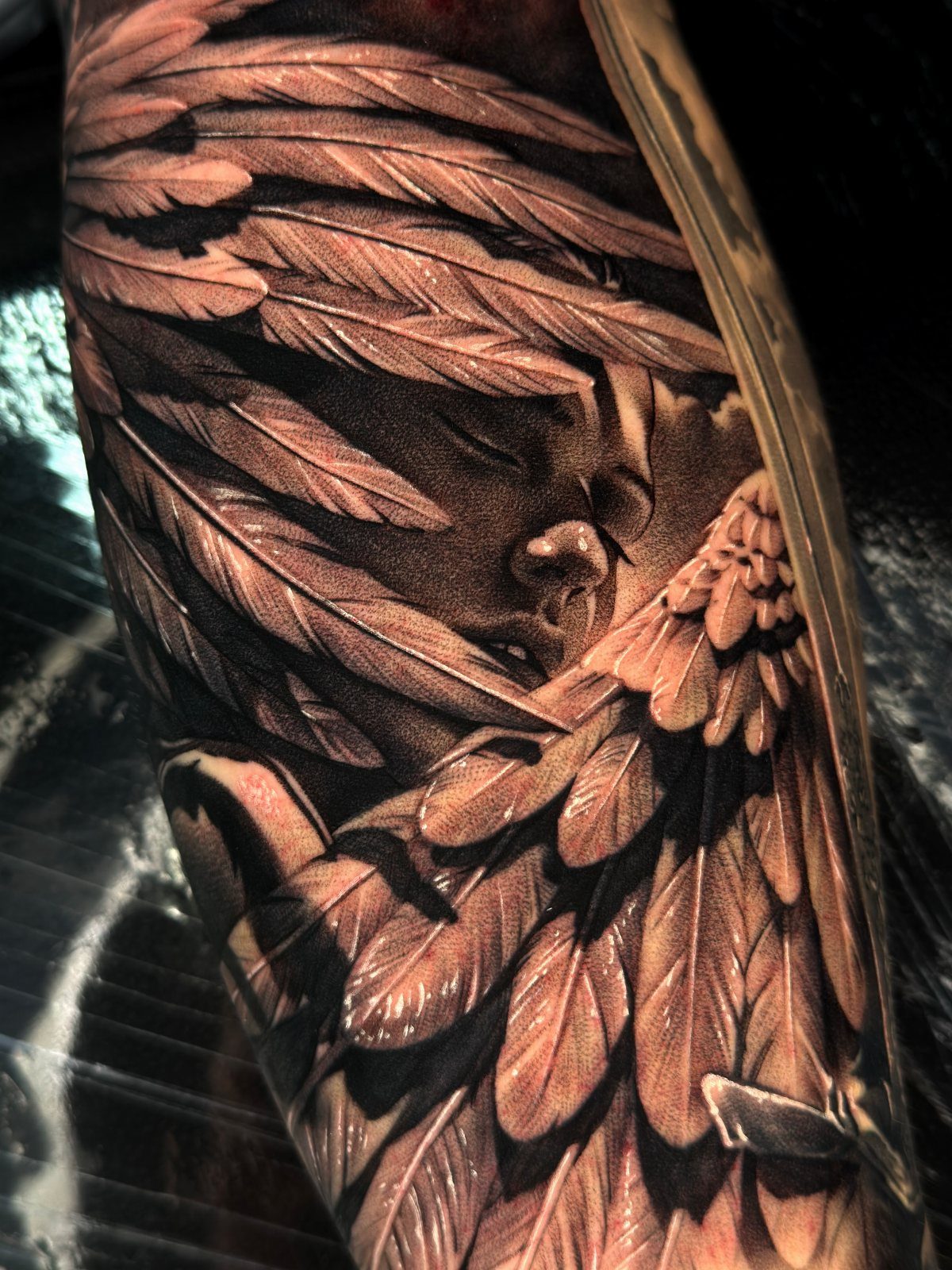 Realistic cherub tattoo with detailed feathers and wings covering part of the face.