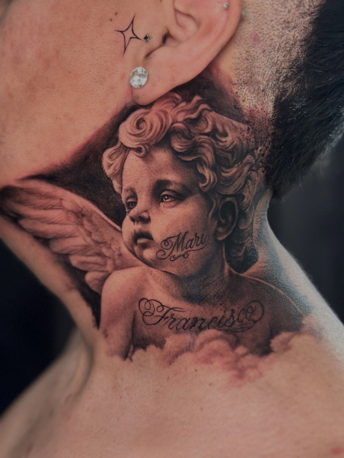 Realistic cherub tattoo on a neck with wings and cursive name scripts.