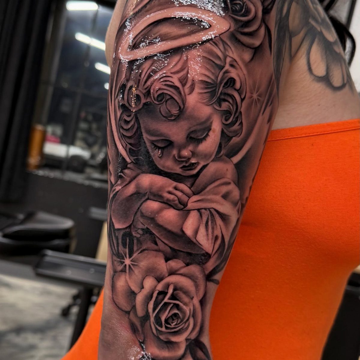 Crying cherub tattoo with a halo and rose on a person's arm