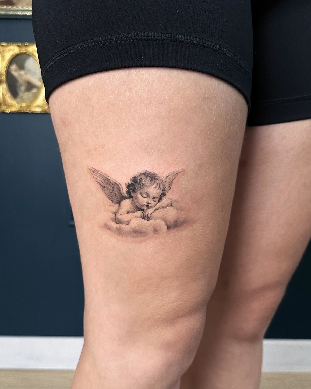Sleeping cherub tattoo on a thigh resting on a soft cloud