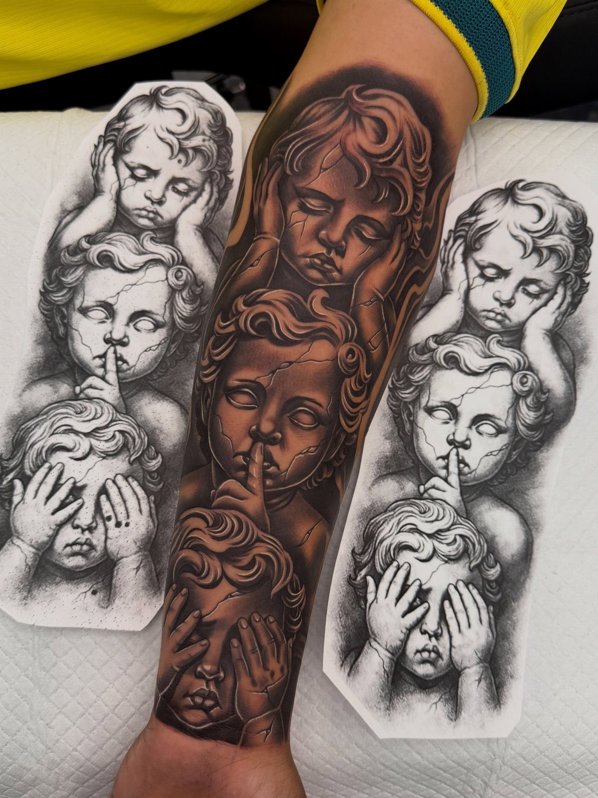 Three cherubs tattoo on a forearm depicting see, hear, and speak no evil.