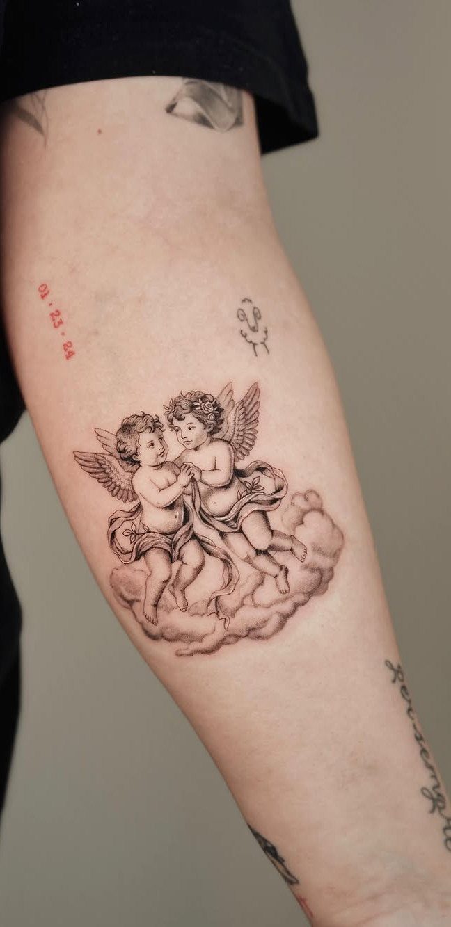 Two cherubs interacting on a cloud as a realistic black and grey arm tattoo.