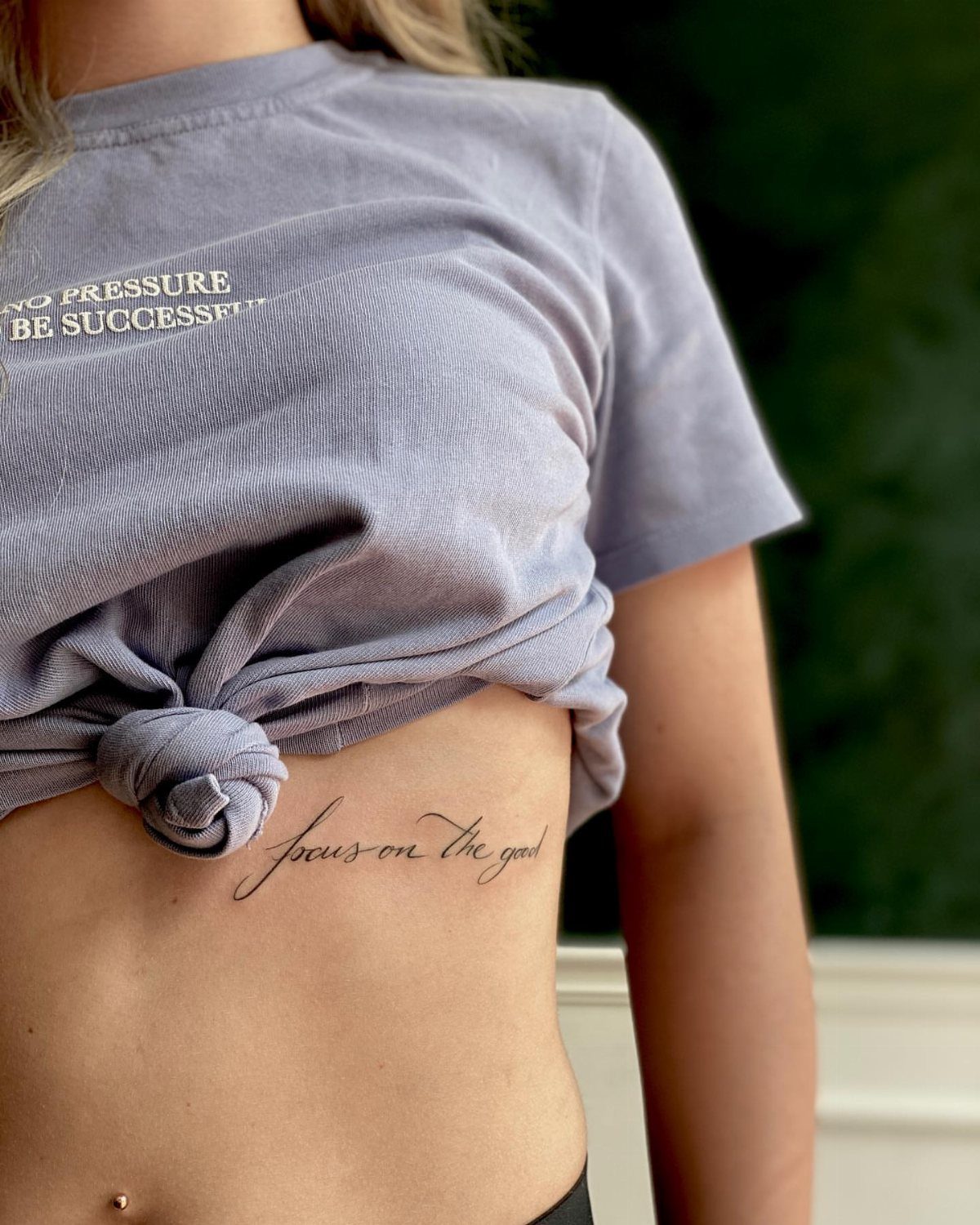 Rib Tattoos for Women: 9 Floral, Celestial and Script Ideas 1 Cursive script tattoo on a woman's ribcage reading focus on the good