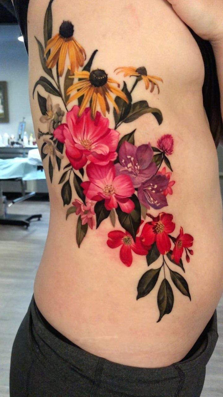 Rib Tattoos for Women: 9 Floral, Celestial and Script Ideas 2 Floral tattoo with yellow, pink, and red flowers on a woman's ribcage.