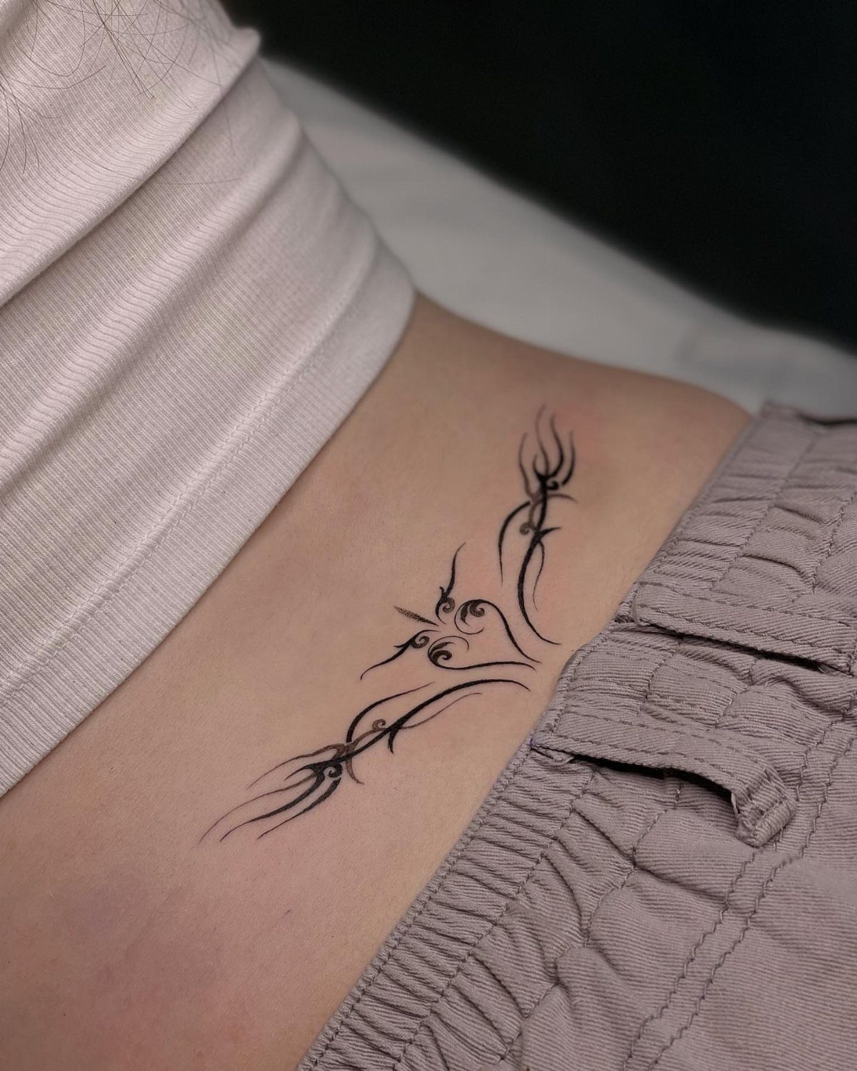 Rib Tattoos for Women: 9 Floral, Celestial and Script Ideas 7 Abstract tribal tattoo with flowing black lines on a person's ribcage