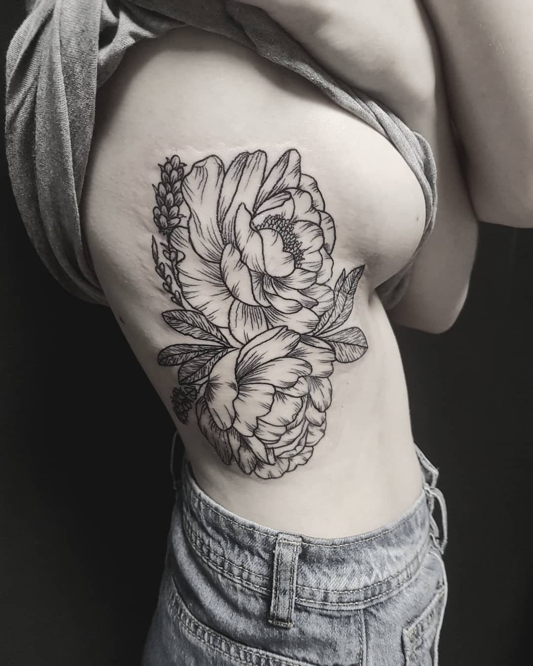 Rib Tattoos for Women: 9 Floral, Celestial and Script Ideas 5 Peony tattoo with detailed petals and leaves on a woman's ribcage.
