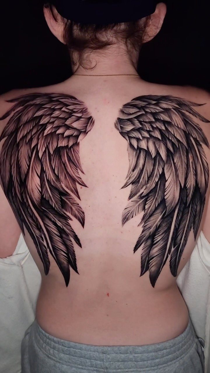 Detailed black and grey angel wing tattoos on a person's back.