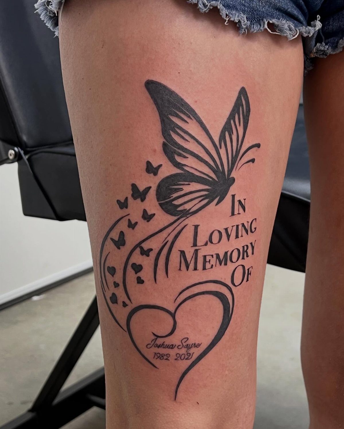Butterfly memorial tattoo on a thigh with a heart and loving memory text.