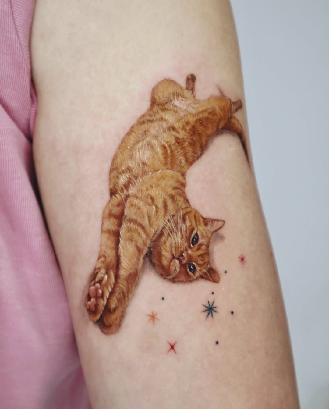 Realistic orange tabby cat tattoo on an arm with small colorful stars.