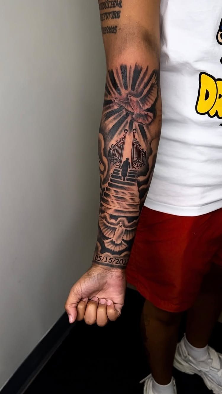 Forearm tattoo featuring a person ascending stairs toward gates with two memorial doves.