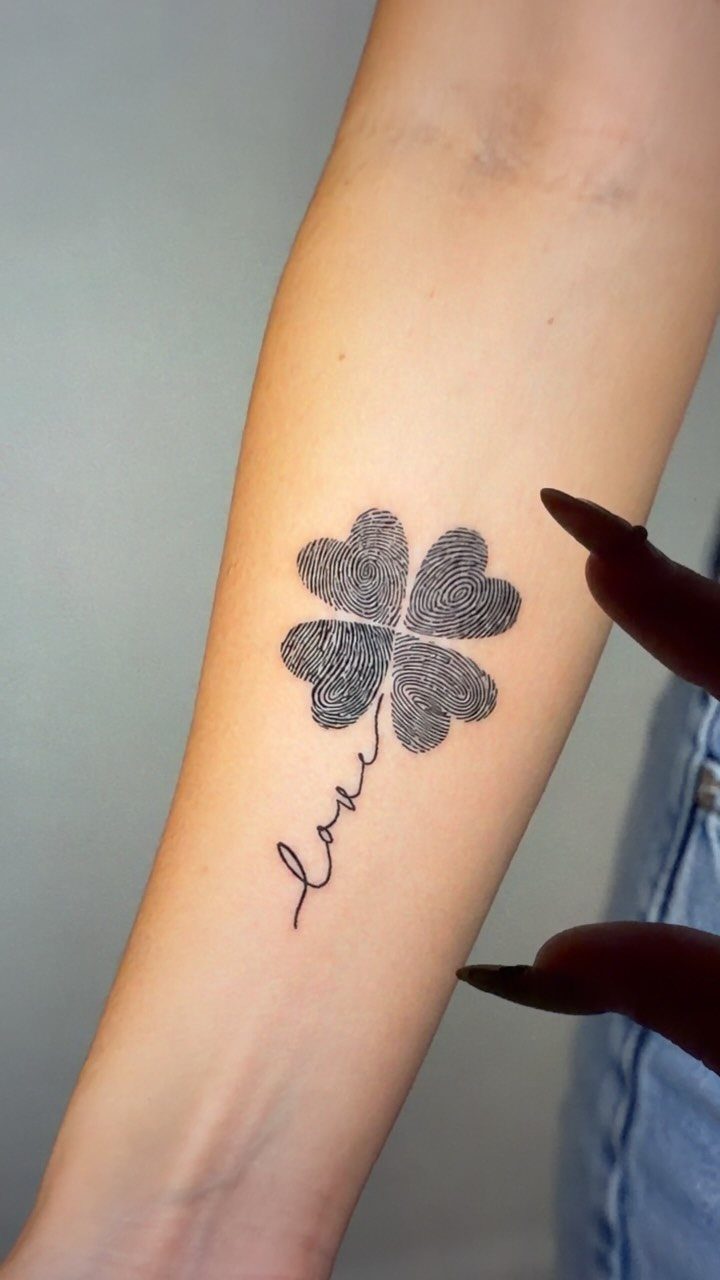 Four-leaf clover tattoo made of fingerprints with the word love as the stem.