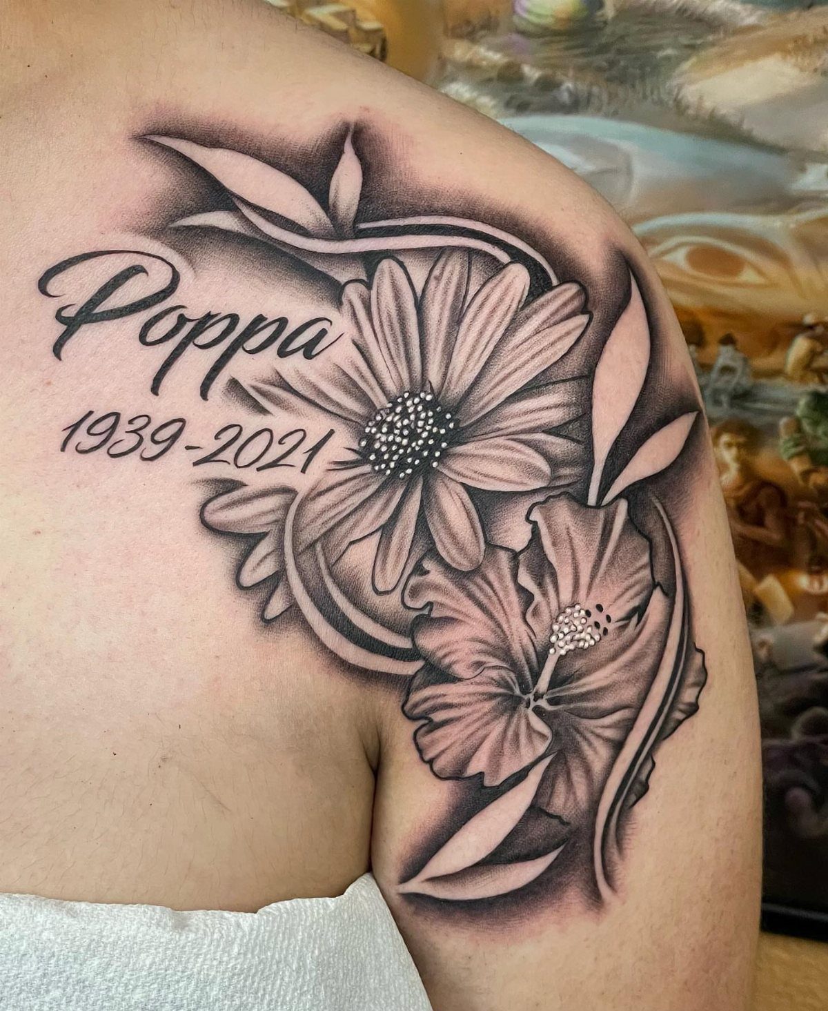 Flower memorial tattoo on a shoulder with the name Poppa and dates 1939-2021.
