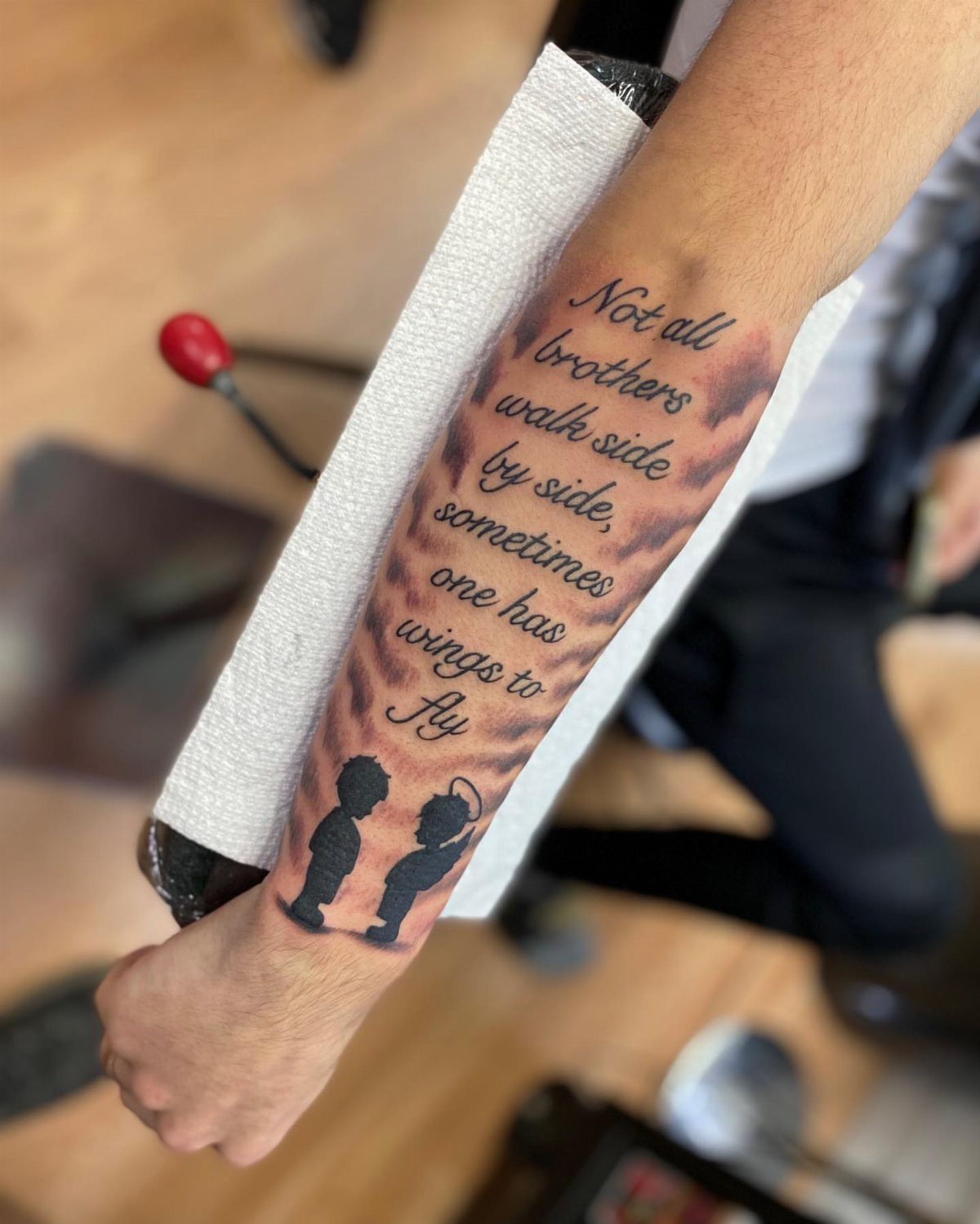 Forearm tattoo with a heartfelt poem about brothers, clouds, and two silhouettes.