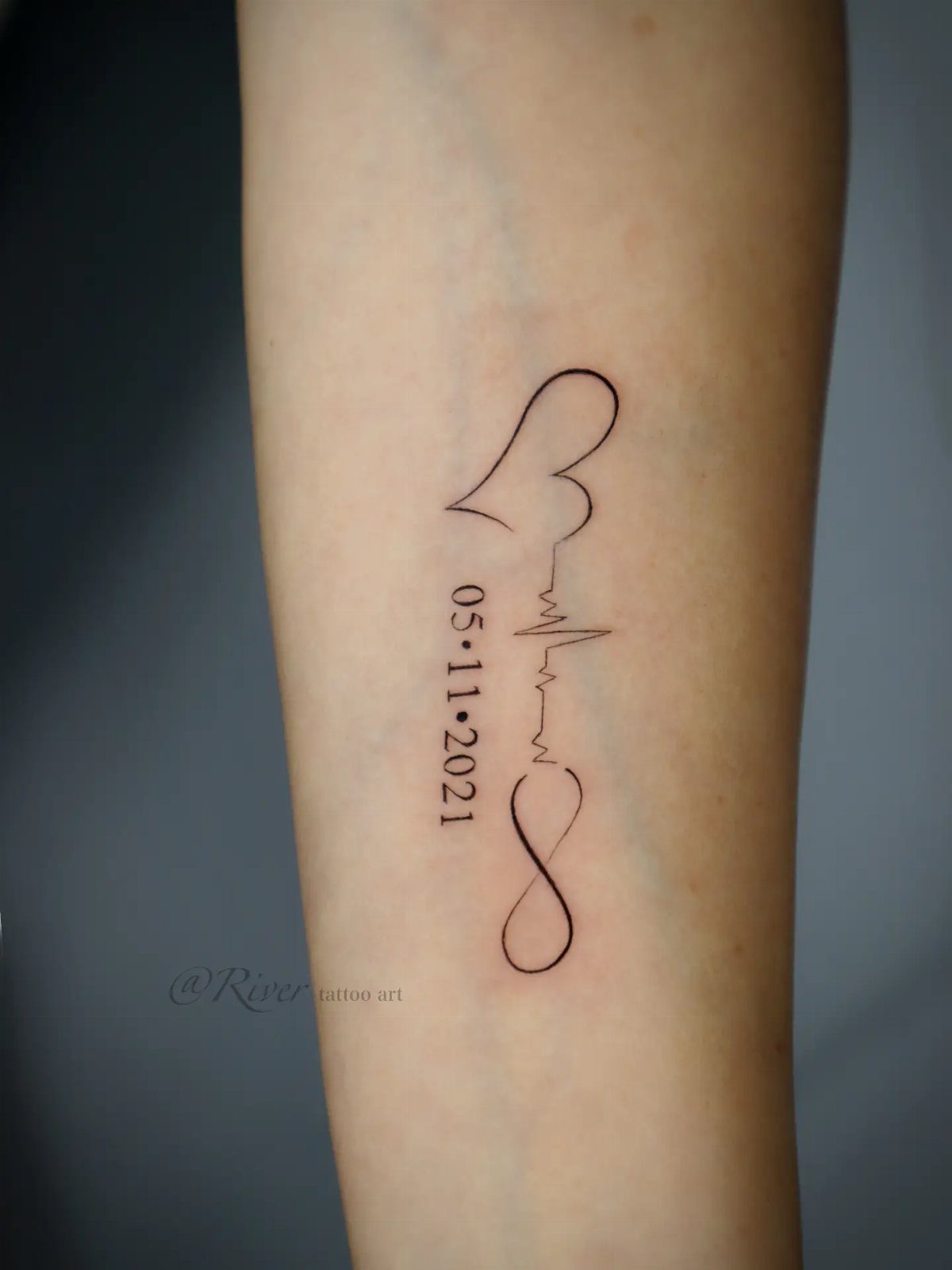 Memorial tattoo on forearm with heart, heartbeat line, date, and infinity symbol.