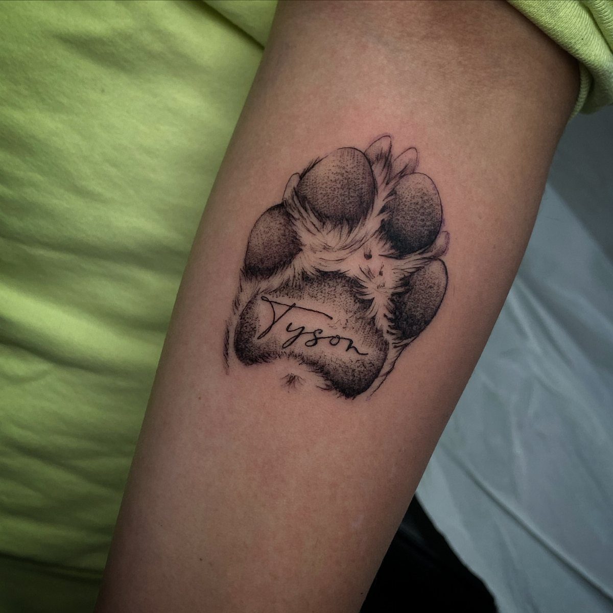 Realistic paw print tattoo on a forearm with the name Tyson in cursive.