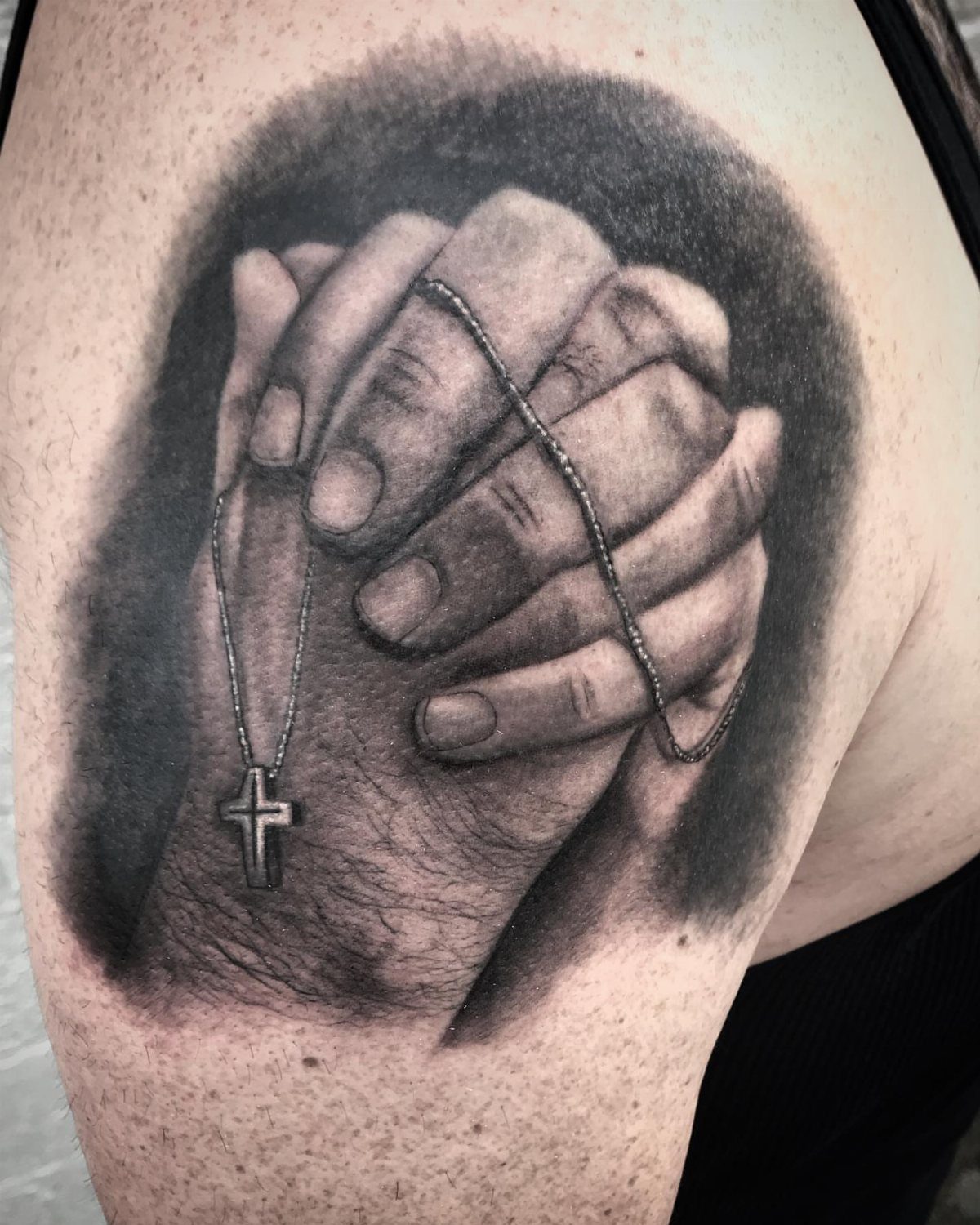 Praying hands tattoo with a rosary and cross on a person's arm.