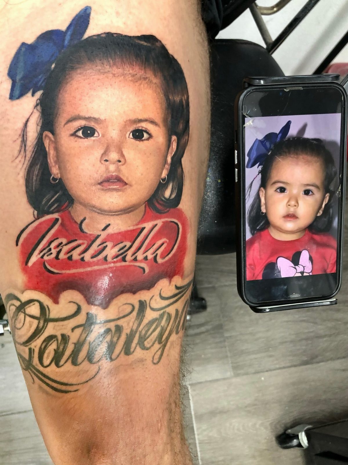 Realistic portrait tattoo of a young girl with a blue bow on a leg.