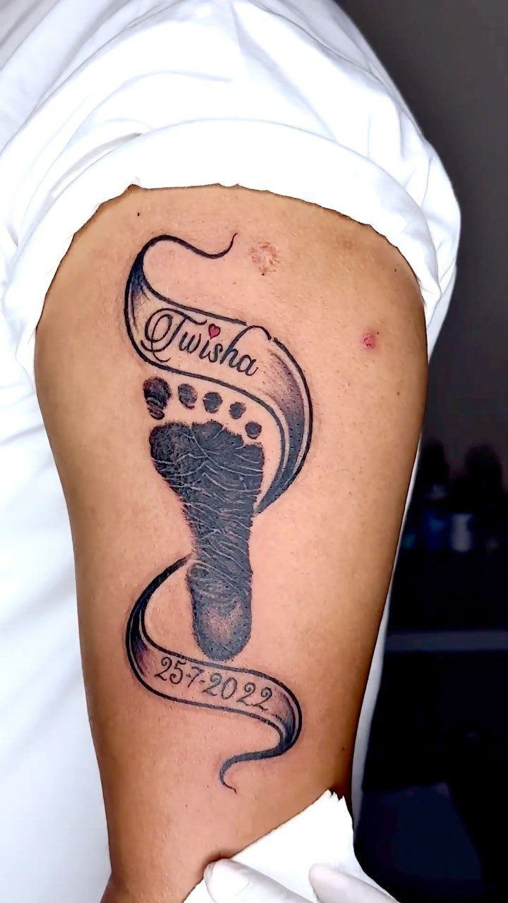 26 Self Tattoo Ideas for Simple, Meaningful Ink 25 Baby footprint tattoo on an arm with ribbons containing a name and date.