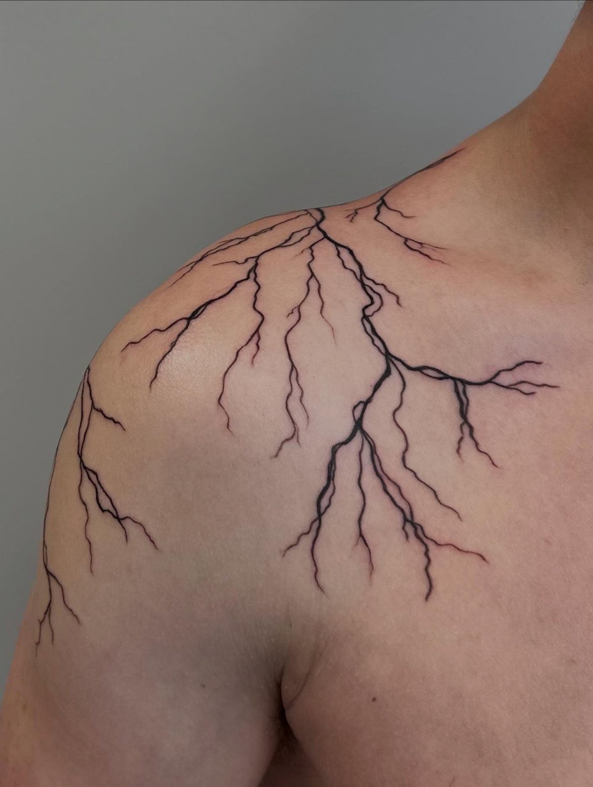 26 Self Tattoo Ideas for Simple, Meaningful Ink 18 Black ink lightning bolt tattoo branching across a person's shoulder and chest.