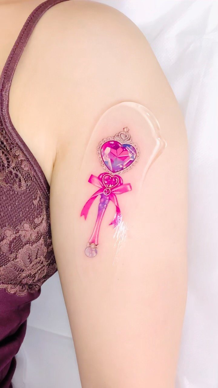 26 Self Tattoo Ideas for Simple, Meaningful Ink 26 Pink heart-shaped magic wand tattoo on a person's upper arm with clear bandage.