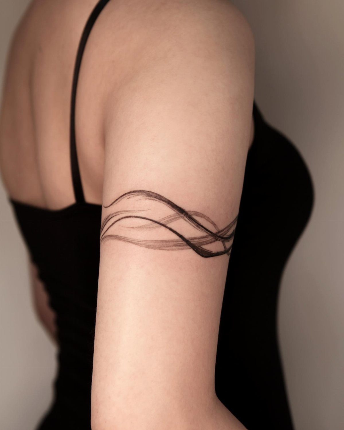 26 Self Tattoo Ideas for Simple, Meaningful Ink 16 Minimalist black ink wave tattoo wrapping around a person's upper arm.