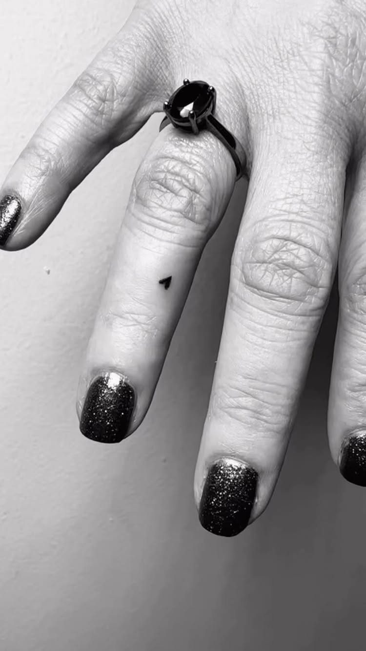 26 Self Tattoo Ideas for Simple, Meaningful Ink 1 Small black heart tattoo on a finger with a ring and glittery nails.