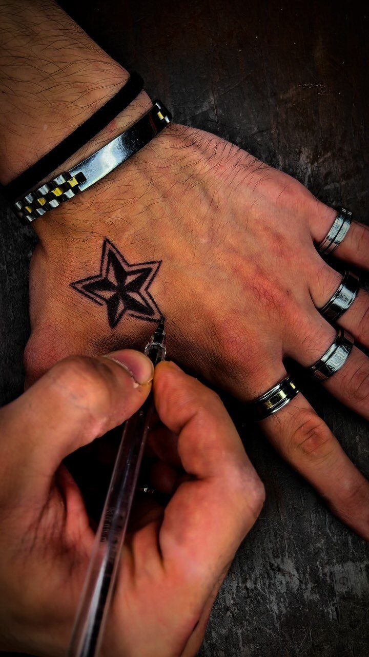 26 Self Tattoo Ideas for Simple, Meaningful Ink 3 Black ink star tattoo being applied to the back of a hand.