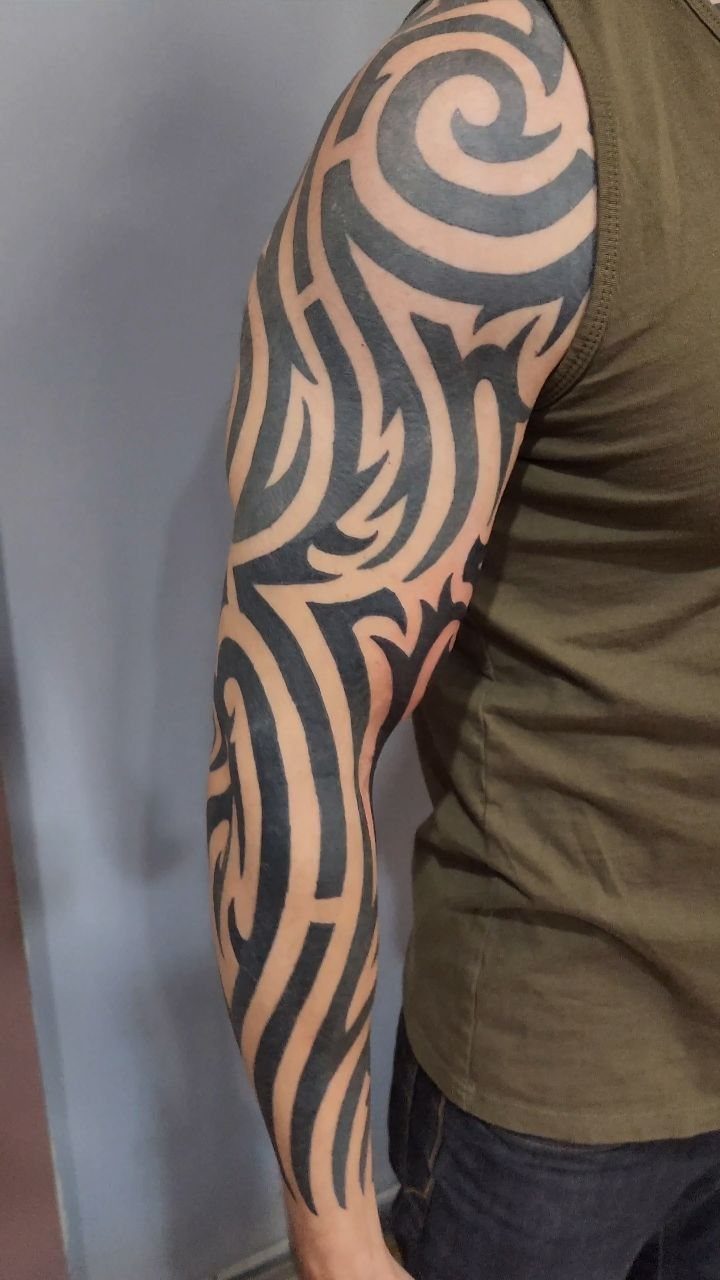 9 Side Arm Tattoos for Animals, Script, Florals and More 8 Tribal tattoo with bold black swirling patterns on a person's arm.