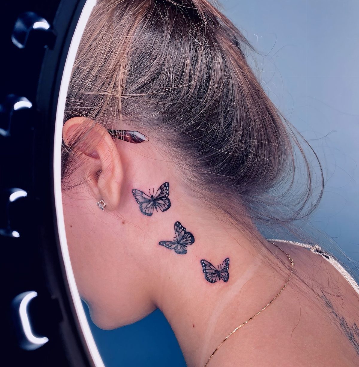 21 Side Neck Tattoo Ideas for Bold, Meaningful Designs 15 Three small black butterfly tattoos arranged vertically on the side of a woman's neck.