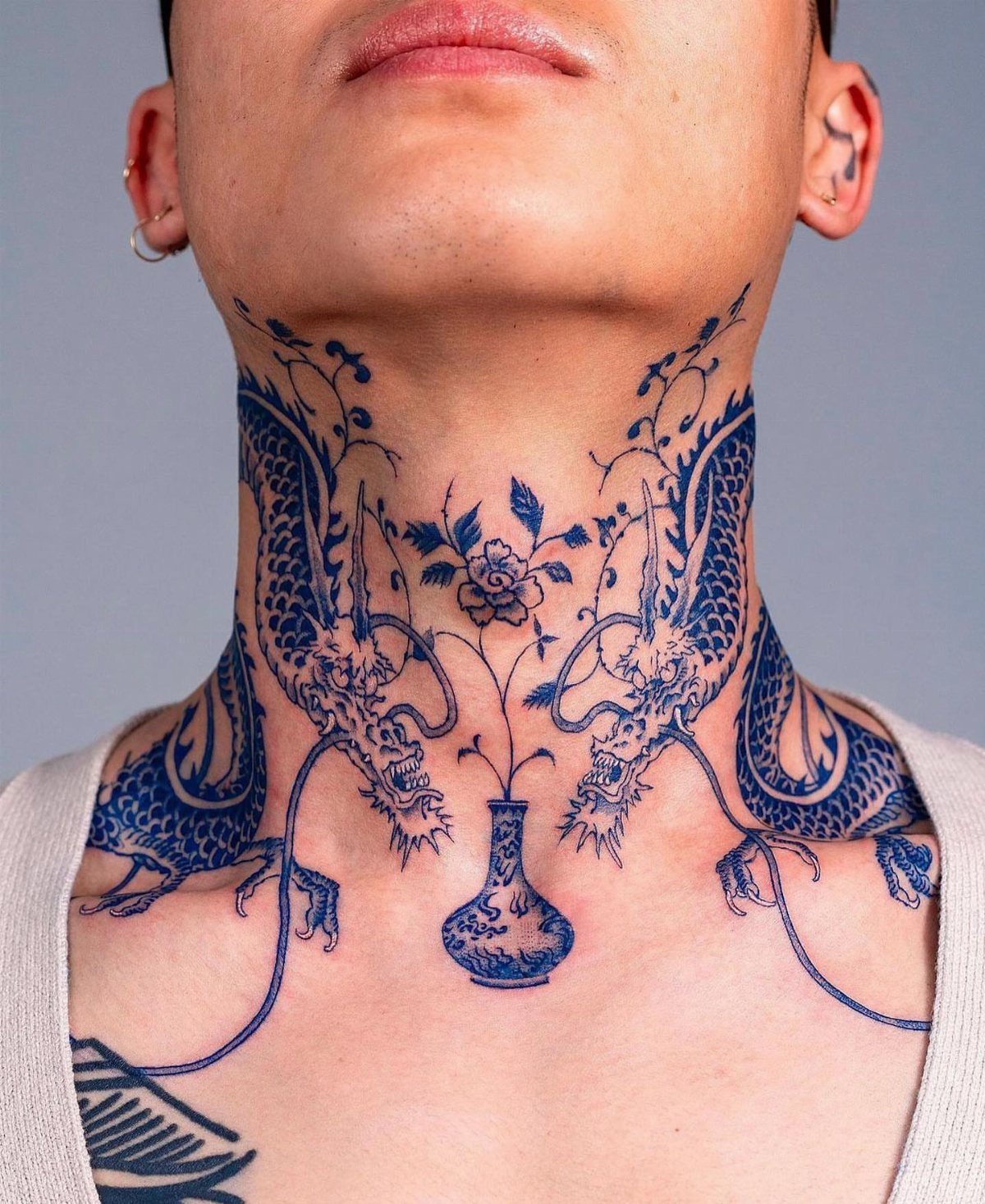 21 Side Neck Tattoo Ideas for Bold, Meaningful Designs 2 Two blue dragons tattooed on a person's neck surrounding a central floral vase.