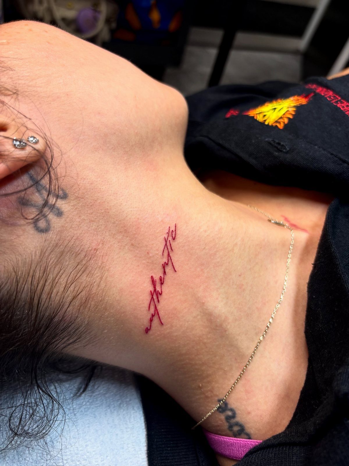 21 Side Neck Tattoo Ideas for Bold, Meaningful Designs 1 Red cursive word tattoo on the side of a person's neck