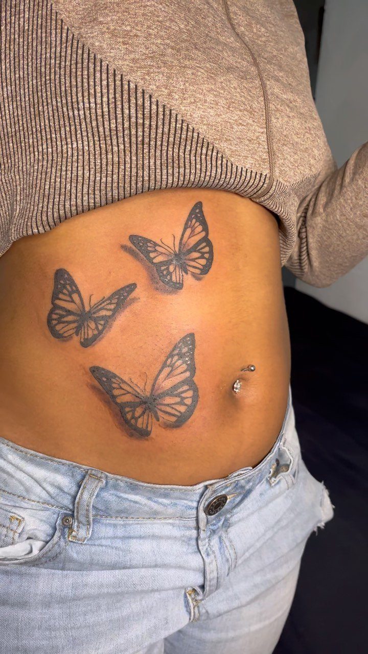 Three butterfly tattoos on a person's side stomach and abdomen area.