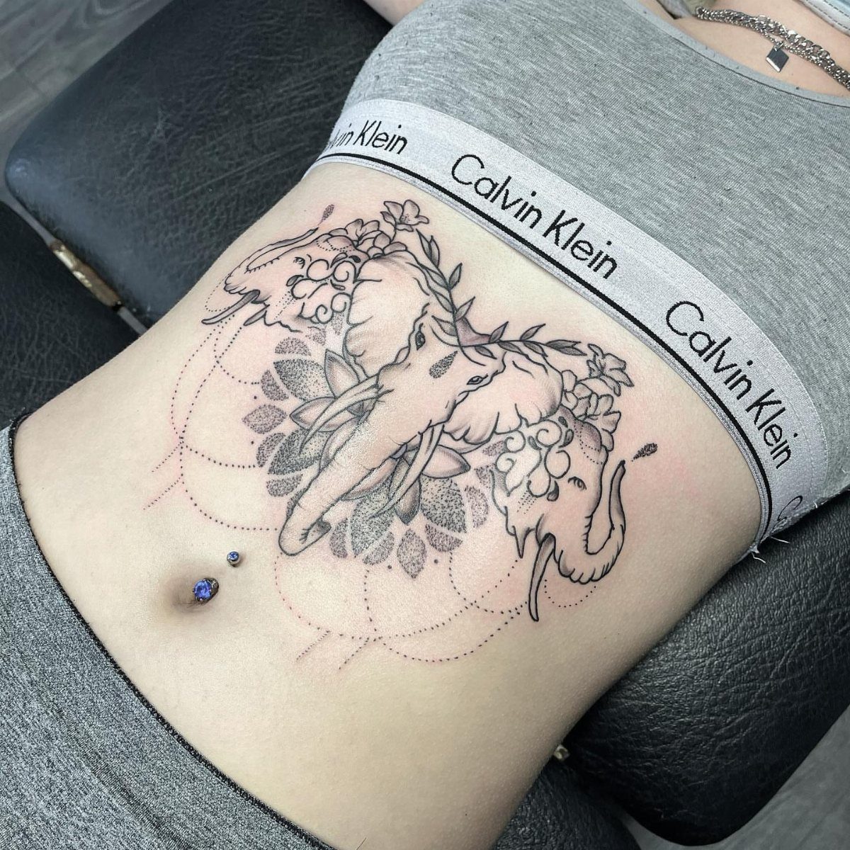 Elephant tattoo with flowers and geometric lines on a person's side stomach