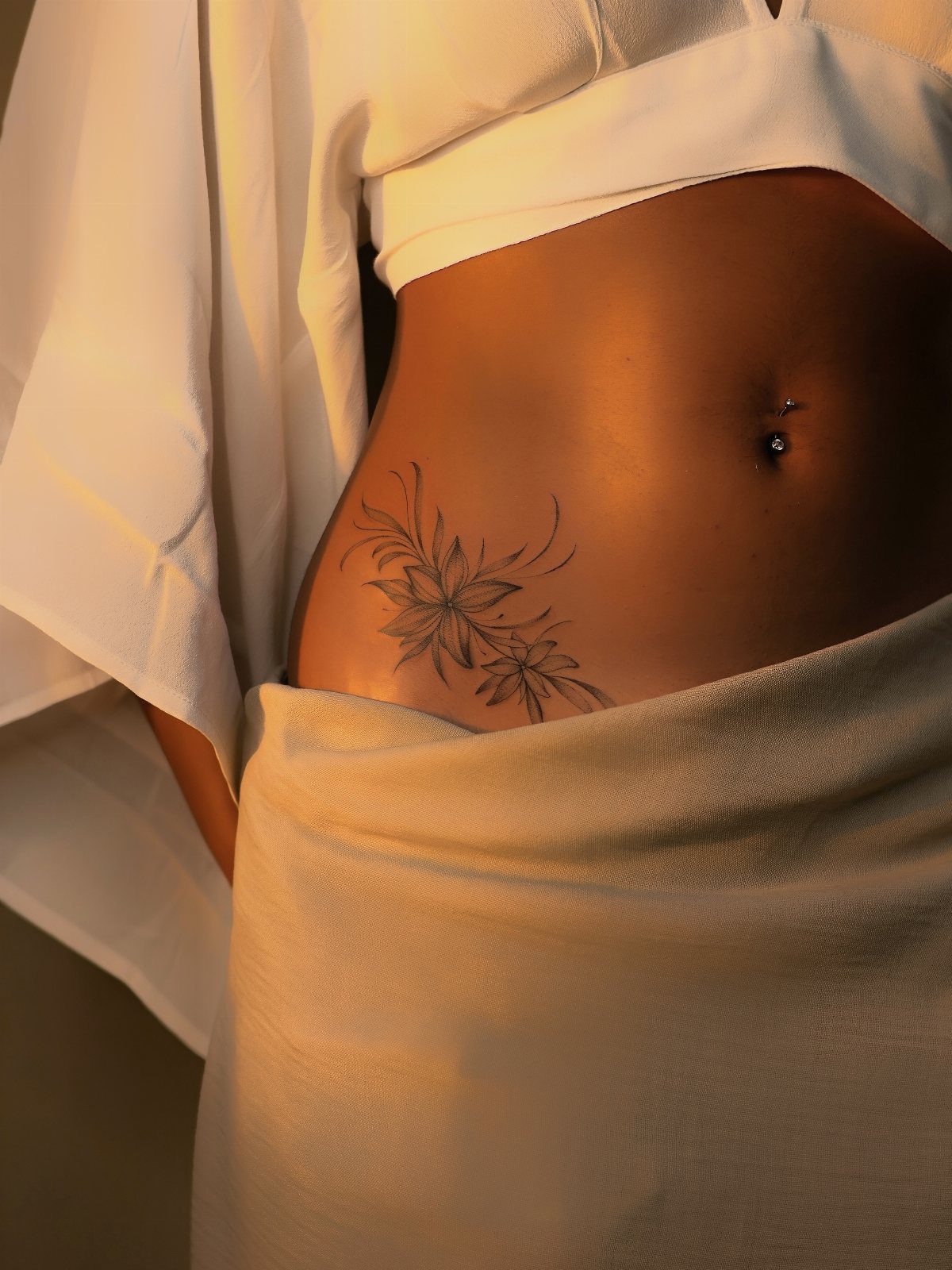 Floral lily tattoo on the side of a person's stomach with white clothing.