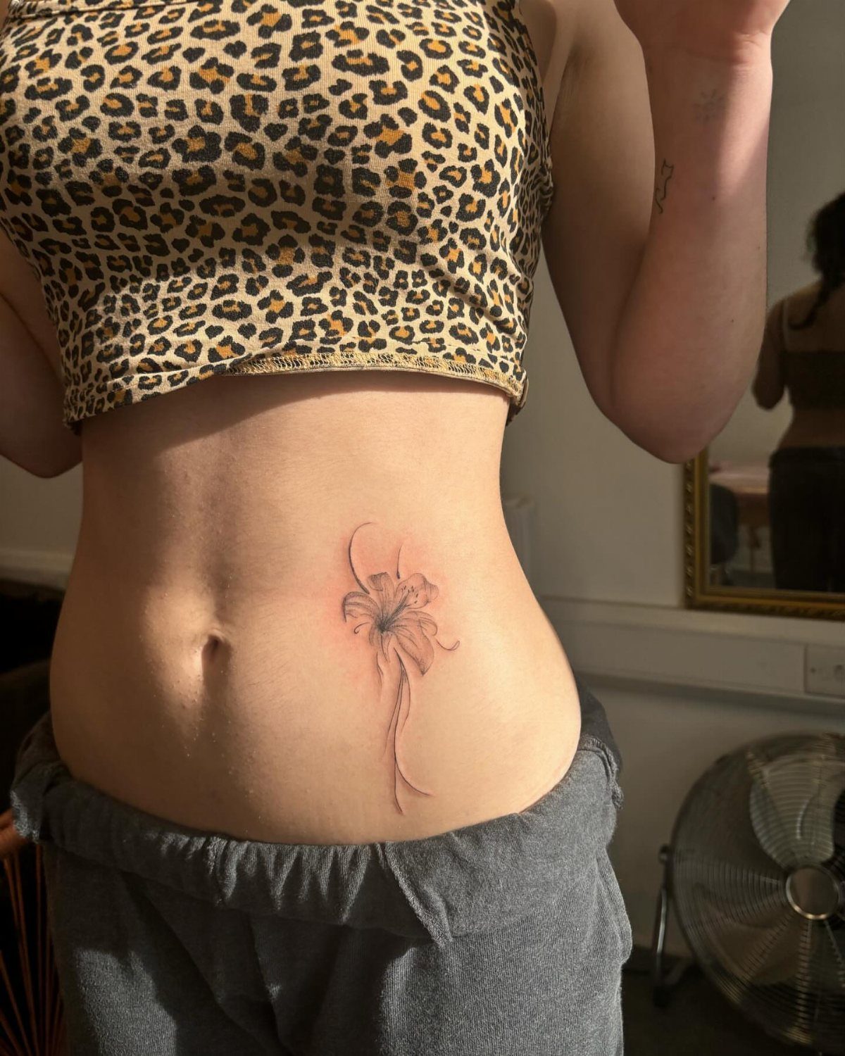 Small red flower tattoo on the side of a person's stomach.