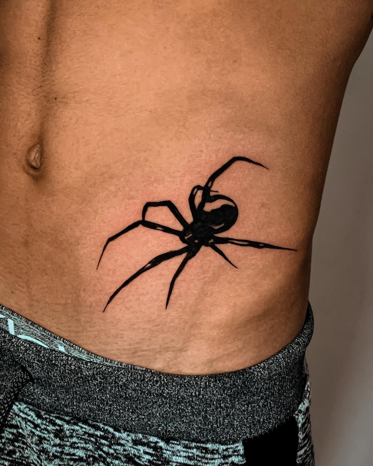 Black spider tattoo on the side of a person's stomach and torso