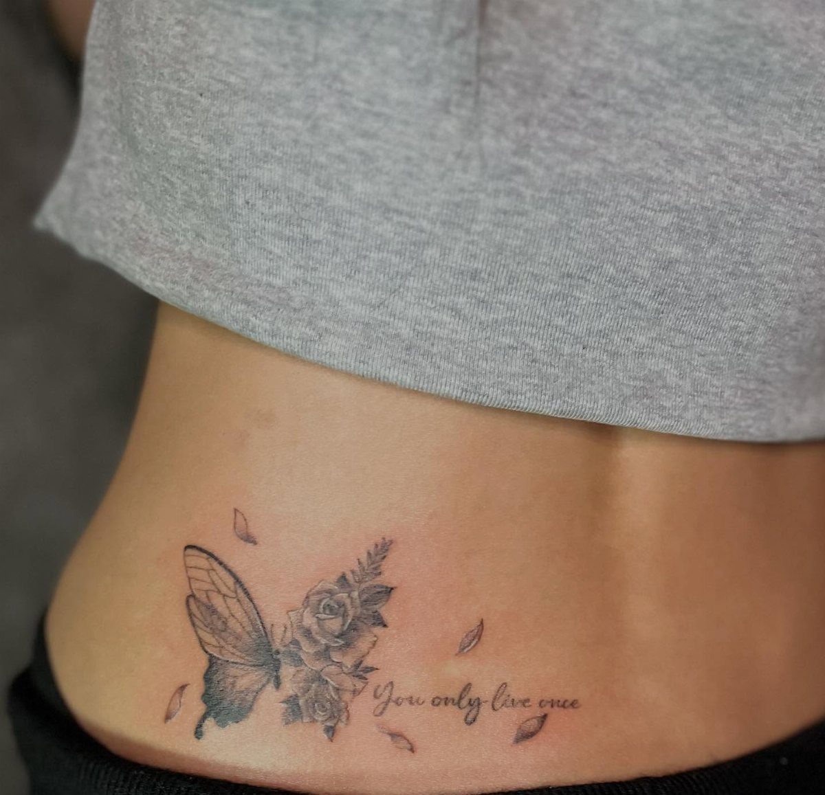 Side stomach tattoo featuring a butterfly, roses, and the phrase You only live once