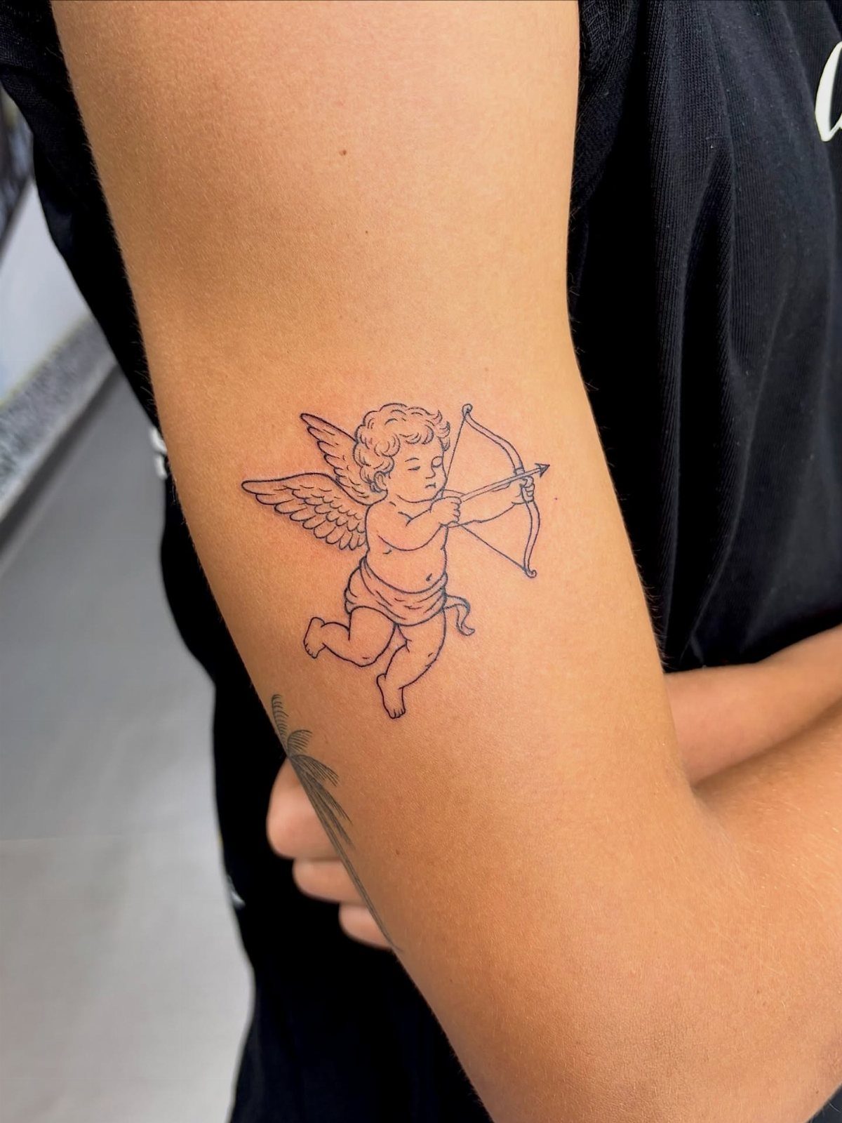 Baby cupid angel tattoo with bow and arrow on an inner bicep