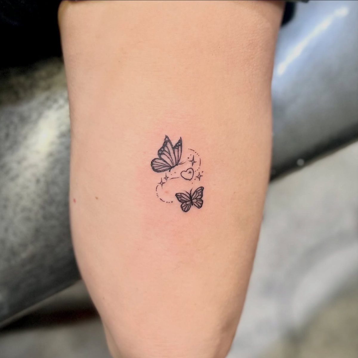 Two small black butterfly tattoos with a heart on a person's inner bicep.