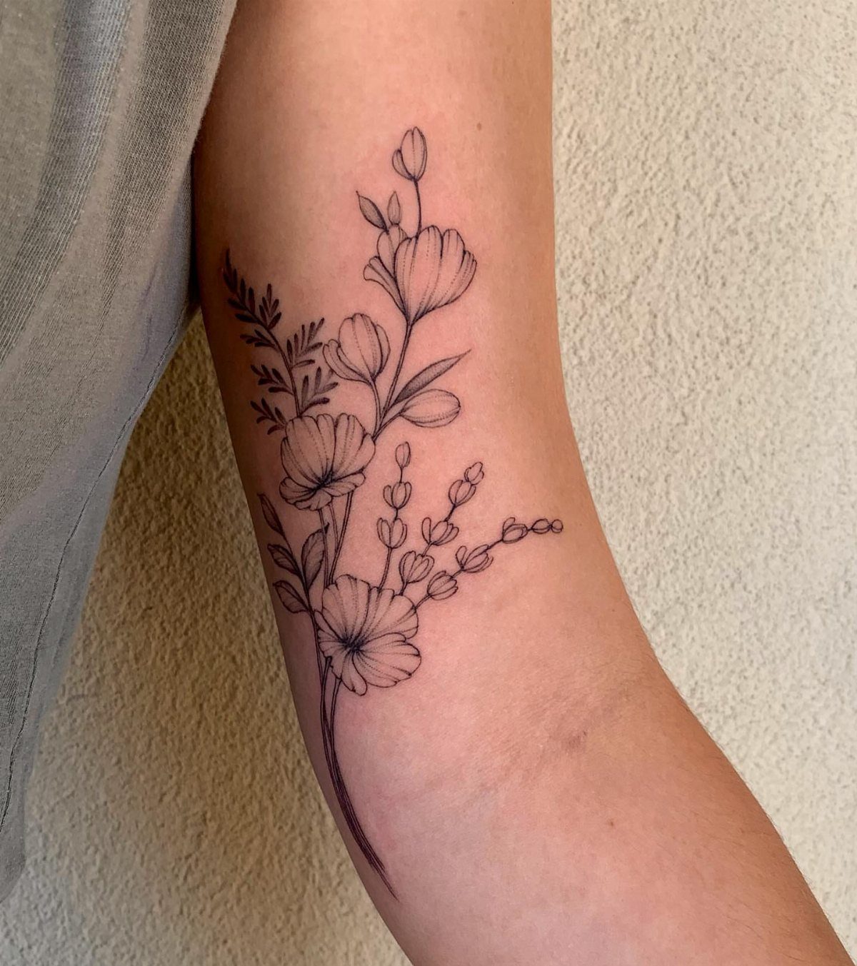 Floral tattoo with delicate flowers and leaves on a person's inner bicep.